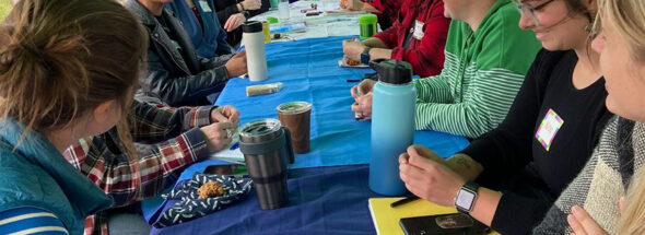 Group of woman sitting around an outdoor table talking and taking notes